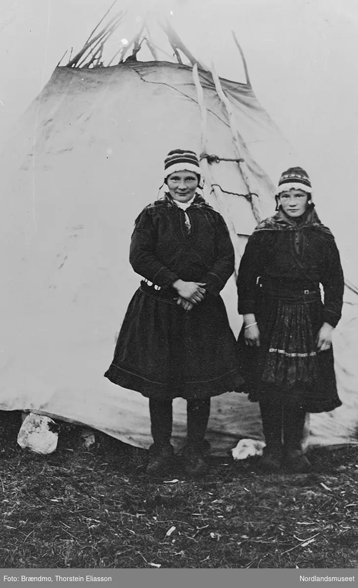 Portrett av 2 samiske kvinner i samedrakt foran et telt. Fra venstre: I. Blind, antagelig svensk lærerinne og søsteren hennes, Maria.