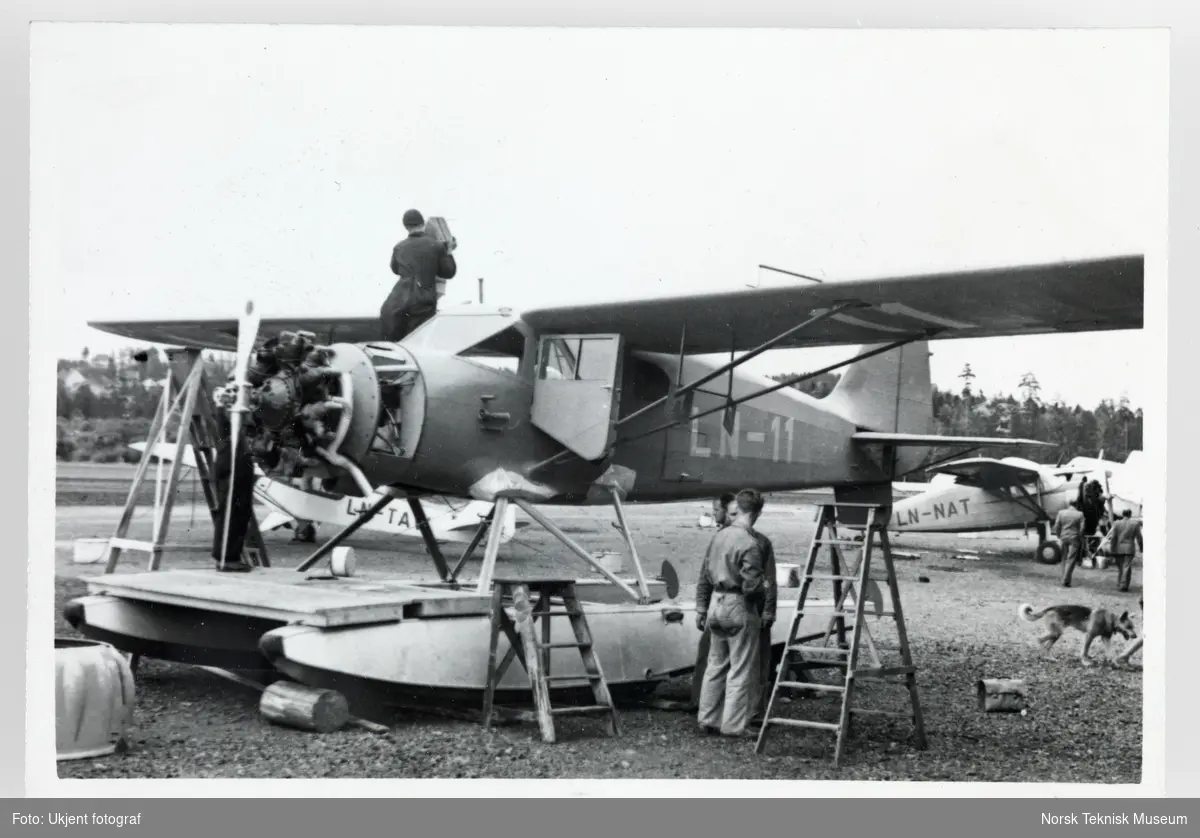 Tre mekanikere arbeider med flyet "Hønningstad C-5 Polar" som står parkert på en slette.