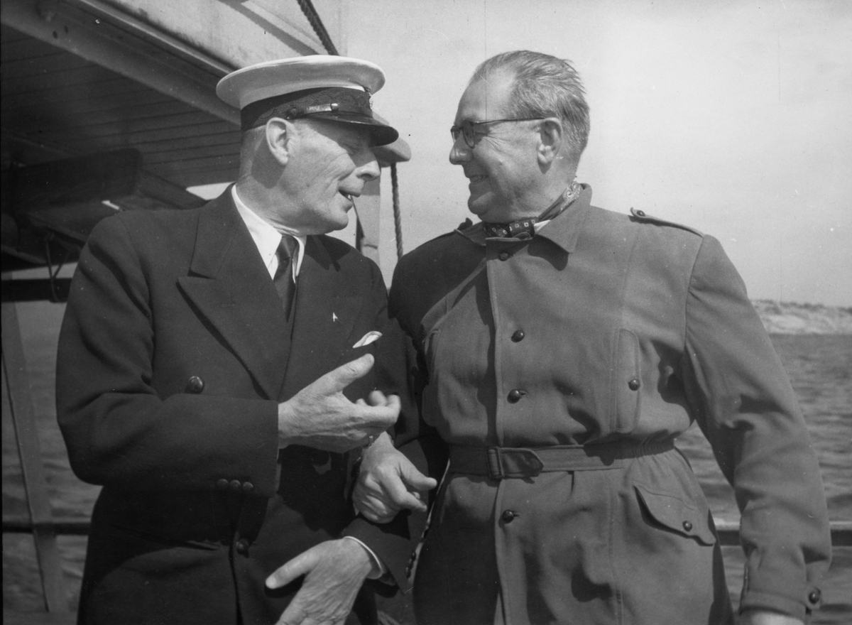 Mannen t v är Gunnar Lund (1884-1973), KSSS-medlem från 1914, under många år funktionär vid sällskapets seglingar, under 1928-46 ledamot av dess tekniska kommitté. Mannen t h har inte kunnat identifieras.