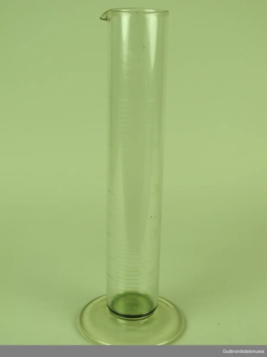 Laboratorieglass med tømmetut, samt måleskala på siden, glasset tar max 50 ml og har tall for hver tiende ml.
Glasset har merke med "Assistent" øverst på glasset.