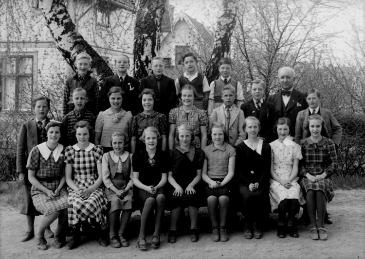 Rynninge skola, 12 flickor, 9 pojkar och lärare Sam. Nystedt på skolgården.
Skolbyggnad i bakgrunden.