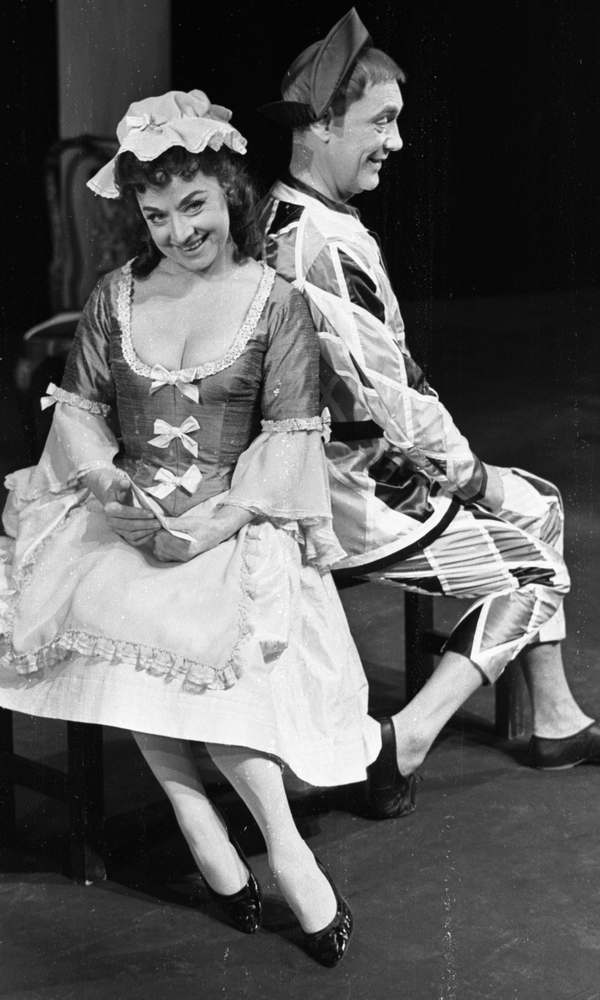 Calle Eriksson, Lustspel på Hjalmar Bergman 5 februari 1966

Två skådespelare, en kvinna och en man, agerar i ett lustspel på Hjalmar Bergmanteatern. De är klädda i 1700-talsinspirerade kläder och sitter tillsammans på en bänk på scenen. Skådespelerskan är klädd i klänning, hatt, strumpor och pumps. Hon håller i ett papper. Skådespelaren har jacka och byxor i rutigt material i Harlekinstil, svarta skor och en trekantig hatt på huvudet.