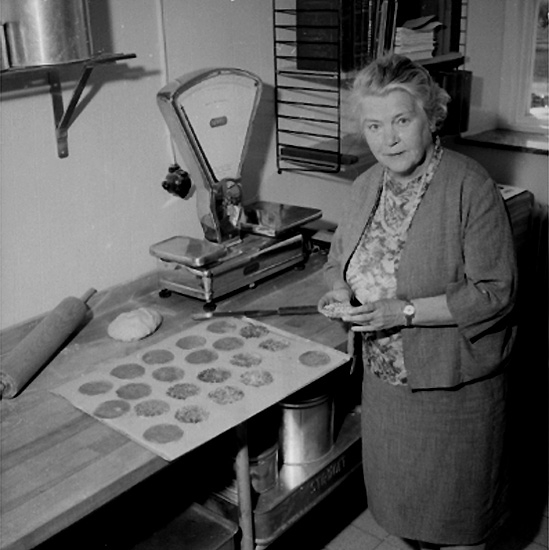 Konsum Bageriet, interiör, en kvinna.
Författaren Margit Palmer-Waldén med "Kajsa Warg kakor".