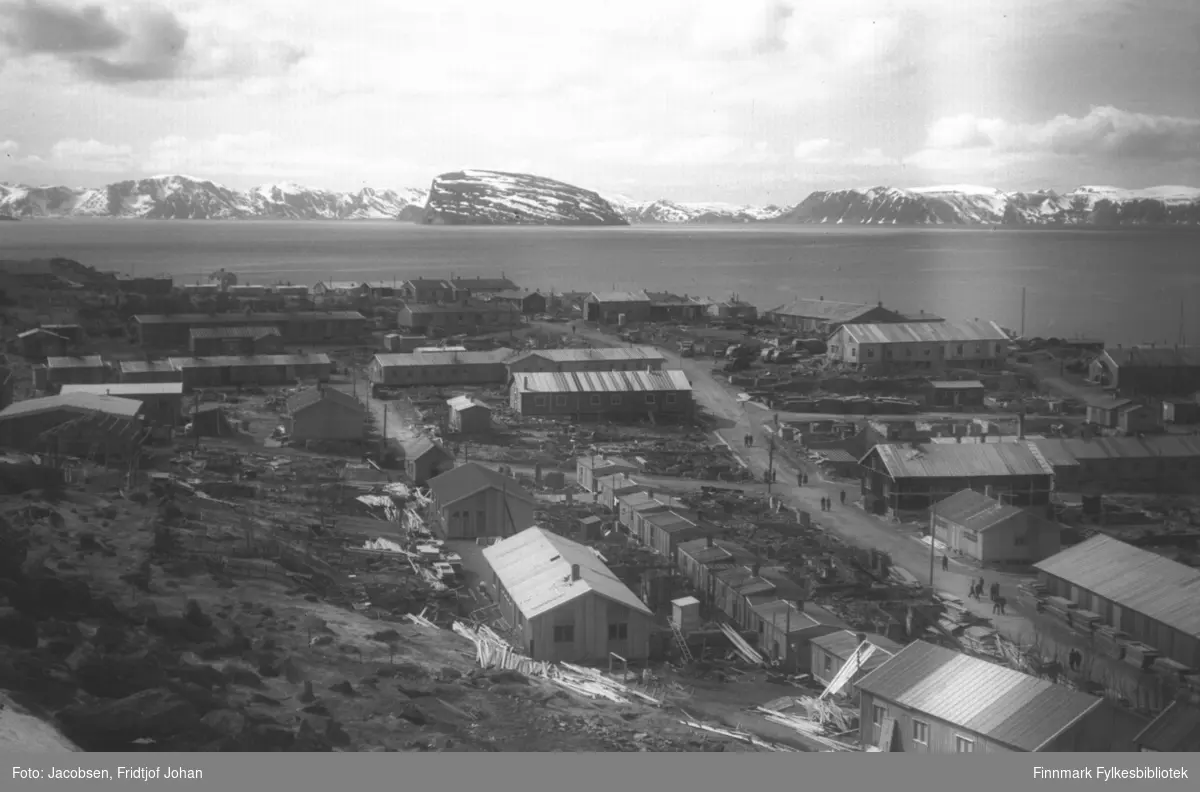 Bydelen Haugen i Hammerfest. Mange brakker, i varierende størrelser og former, er satt opp på området. Gata der det er en del folk som går er Randebakken. Telegrafbrakka ligger til helt til høyre cirka midt på bildet med røstveggen ut mot Randebakken. Kirkegården ses oppe til venstre på bildet. Havområdet er Sørøysundet med innseilingen til Hammerfest helt til venstre på bildet. Øya Håja og enden av Hjelmen ses midt på bildet og bak de ligger Sørøya. En del snøflekker og snø på toppene tyder å at bildet er tatt om våren.