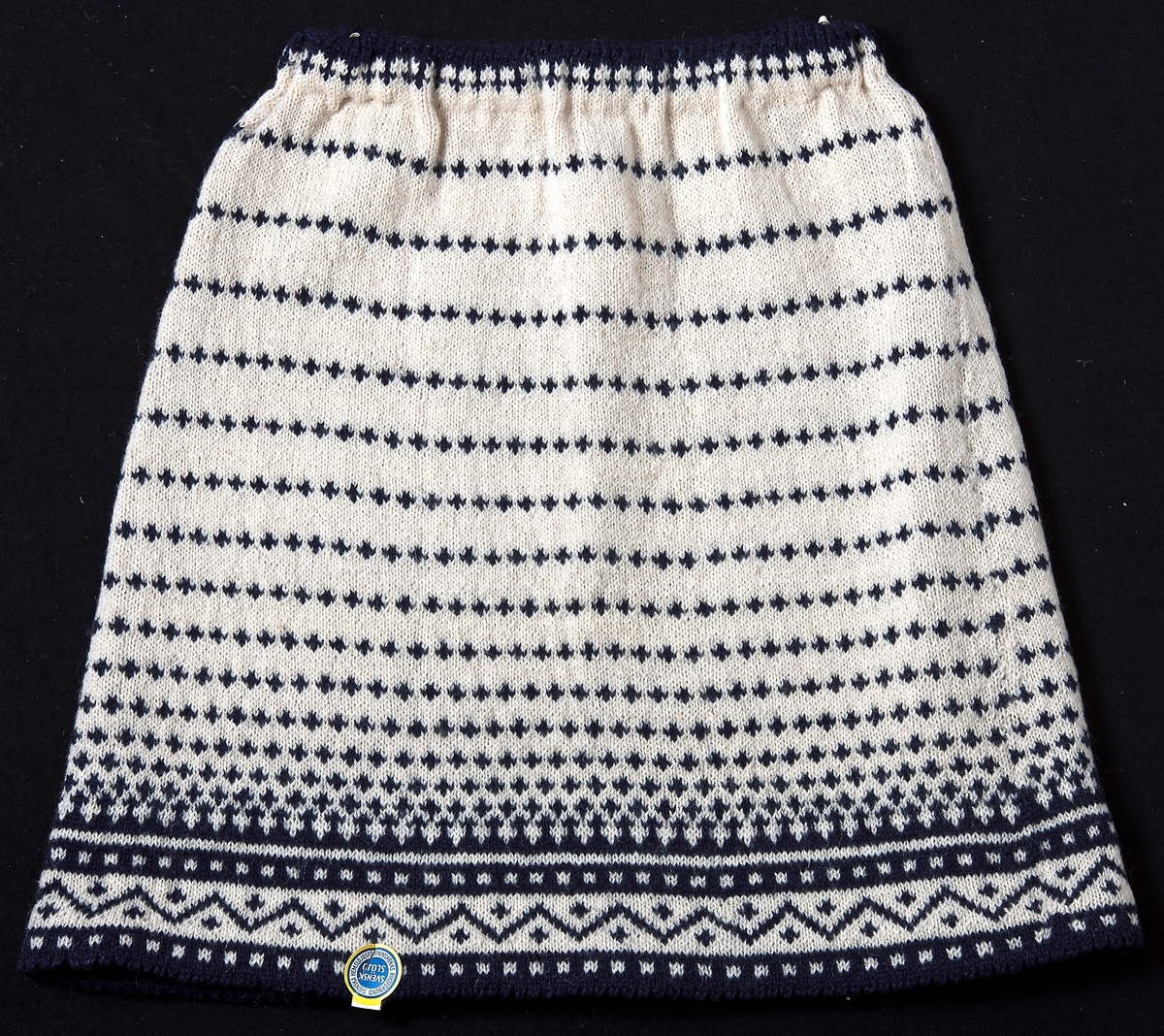 Kjol stickad i Bingestickning i färgerna naturvit och blå med tvåtrådigt ullgarn. Kjolen har en resårlinning.