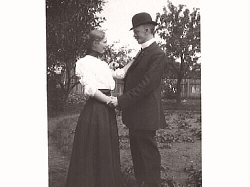 Finklätt ungt par fotograferade utomhus i en trädgård eller park inhägnad med trästaket. De heter Amelie och Johan Winqvist (bror till fotografen).