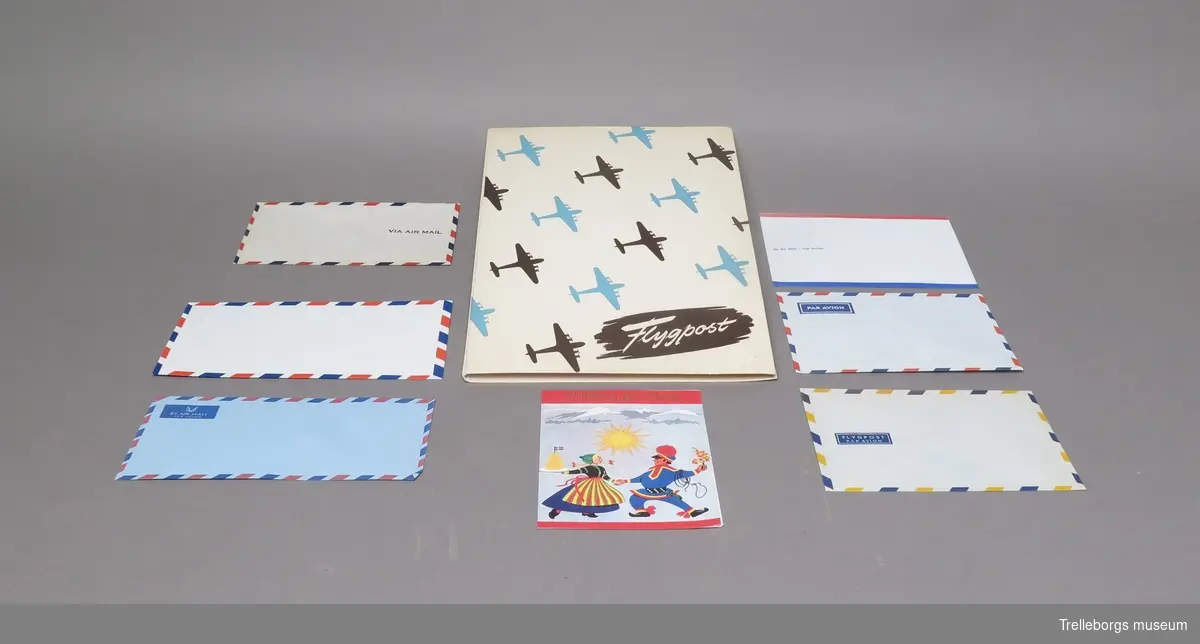 En mapp innehållande skrivpapper och kuvert. Mappen är vit med bruna och ljusblå flygplan, samt ett brunt fält med vit text.