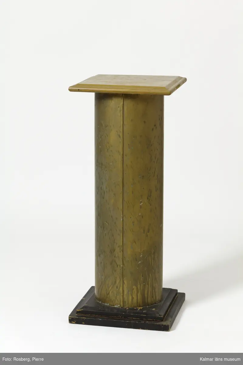 KLM 28494:113. Piedestal. Av trä och metall, plåt. Formad som en kolonn med skaft i bemålad plåt med guldfärg, samt med motiv av blommande fruktträdsgrenar i rosa och grönt, med en fjäril. Basplatta och överdel i kvadratisk form av trä, i svart respektive beige färg.