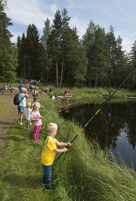 Bildet viser barn som står å fisker i fiskedammen.