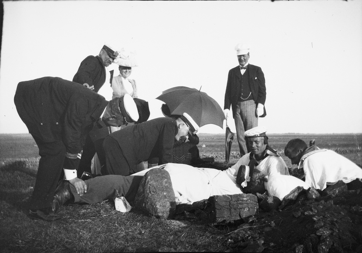 Drottning Victorias bilder. Utgrävning av forngrav på Öland. Riksantikvarie Hans Hildebrand ligger med huvudet ner i gropen.