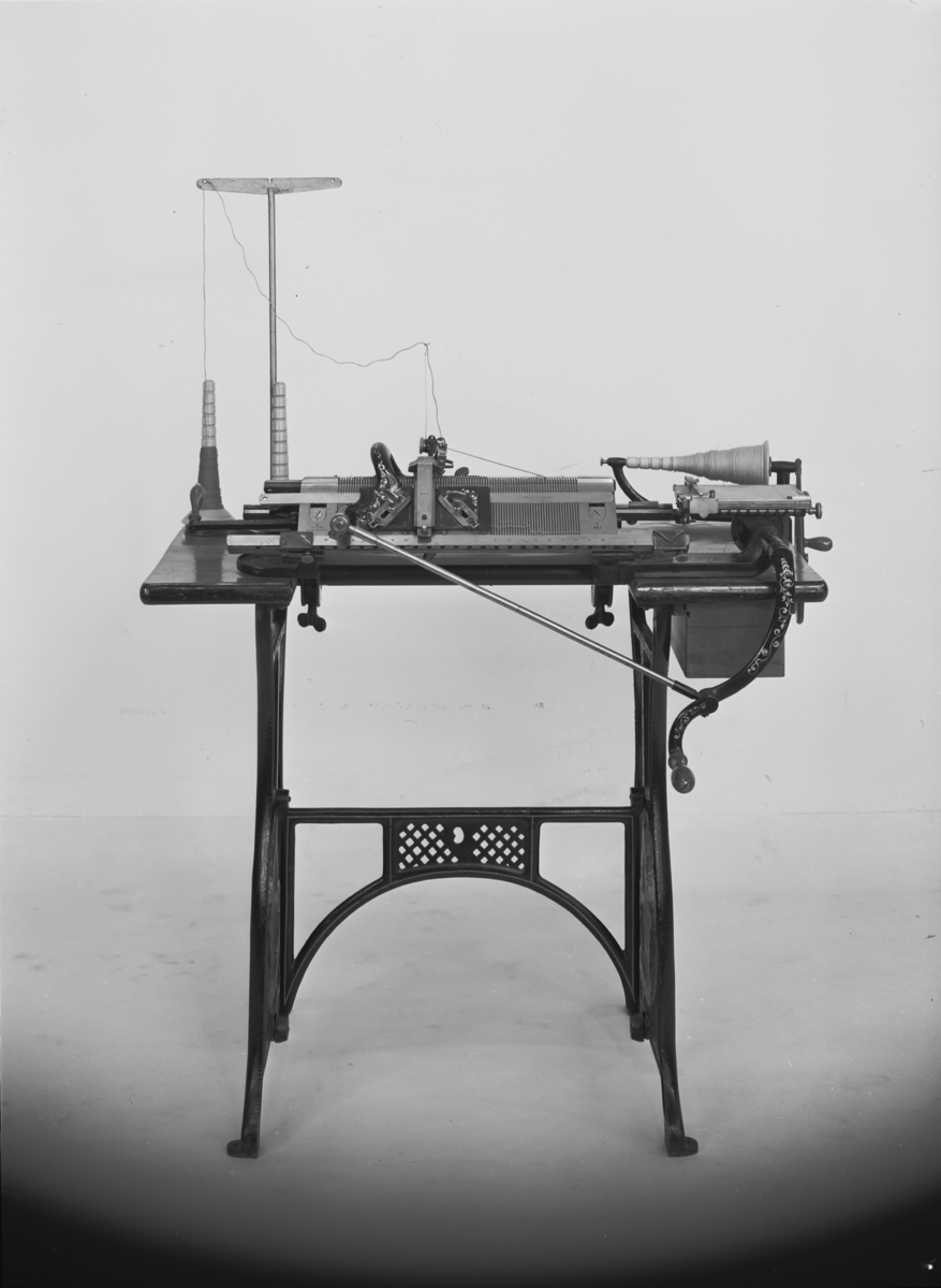 Väv och stickmaskin, "Hemtomten", enligt Per Perssons patent. Jämte tillbehör. Denna maskin är av klass VI (med 6 nålar per engelsk tum) med 176 nålar (35 cm nålrum).
Tillbehör: Lösa tillbehör: 2 st. vikthållare med krok, 2 st. mindre vikter, 2 st. större vikter, 1 st. uppläggningskam (med ståltråd), 1 st. stäckare, 1 st. vikt me vass krok att fästa i arbetet. 10 st. olika verktyg och andra tillbehör.