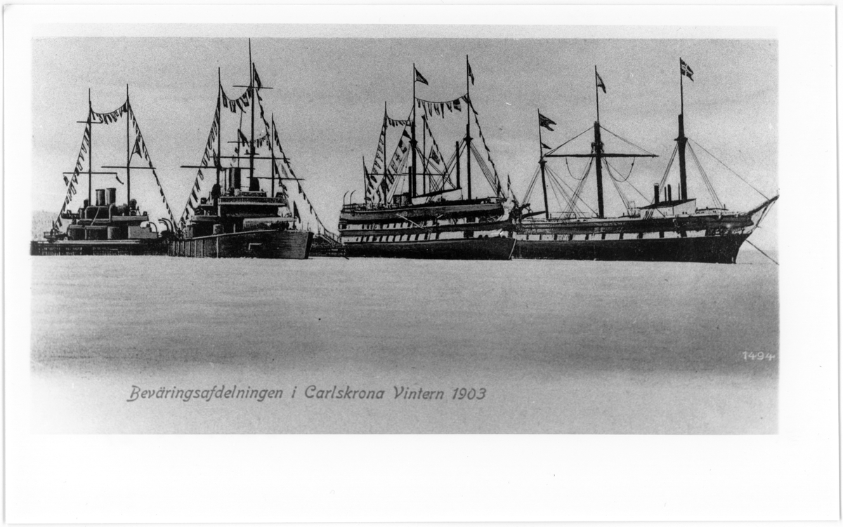 Bilden visar fyra svenska örlogsfartyg som ligger förtöjt bredvid varandra i Karlskronas hamn vinter 1903. Mellan fartygen syns den gamla klaffbron. De två segelfartyg är nedriggade och ombyggd till logementsfartyg. Alla fartyg är flaggad.