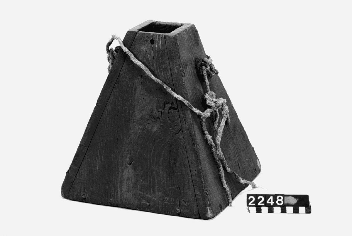 Krutflaska av trä, pyramidformig med handtag av rep.