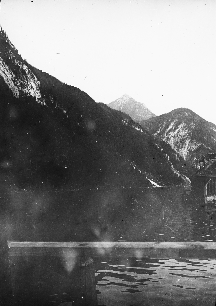 Skioptikonbild med motiv av fjällsjön Königssee i sydöstra Beyern.
Bilden har förvarats i kartong märkt: Höstresan 1909.Köningssee 3. München 1. Innsbruck 3. No: 13. Text på bild: "Der Köningssee".