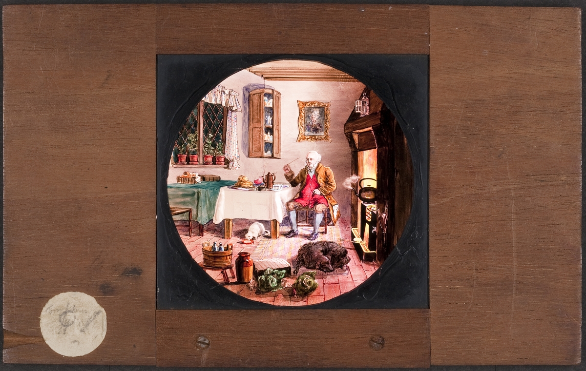 Ljusbild för laterna magica med motiv av äldre man i sitt kök, vid spisen med sin hund och katt.
