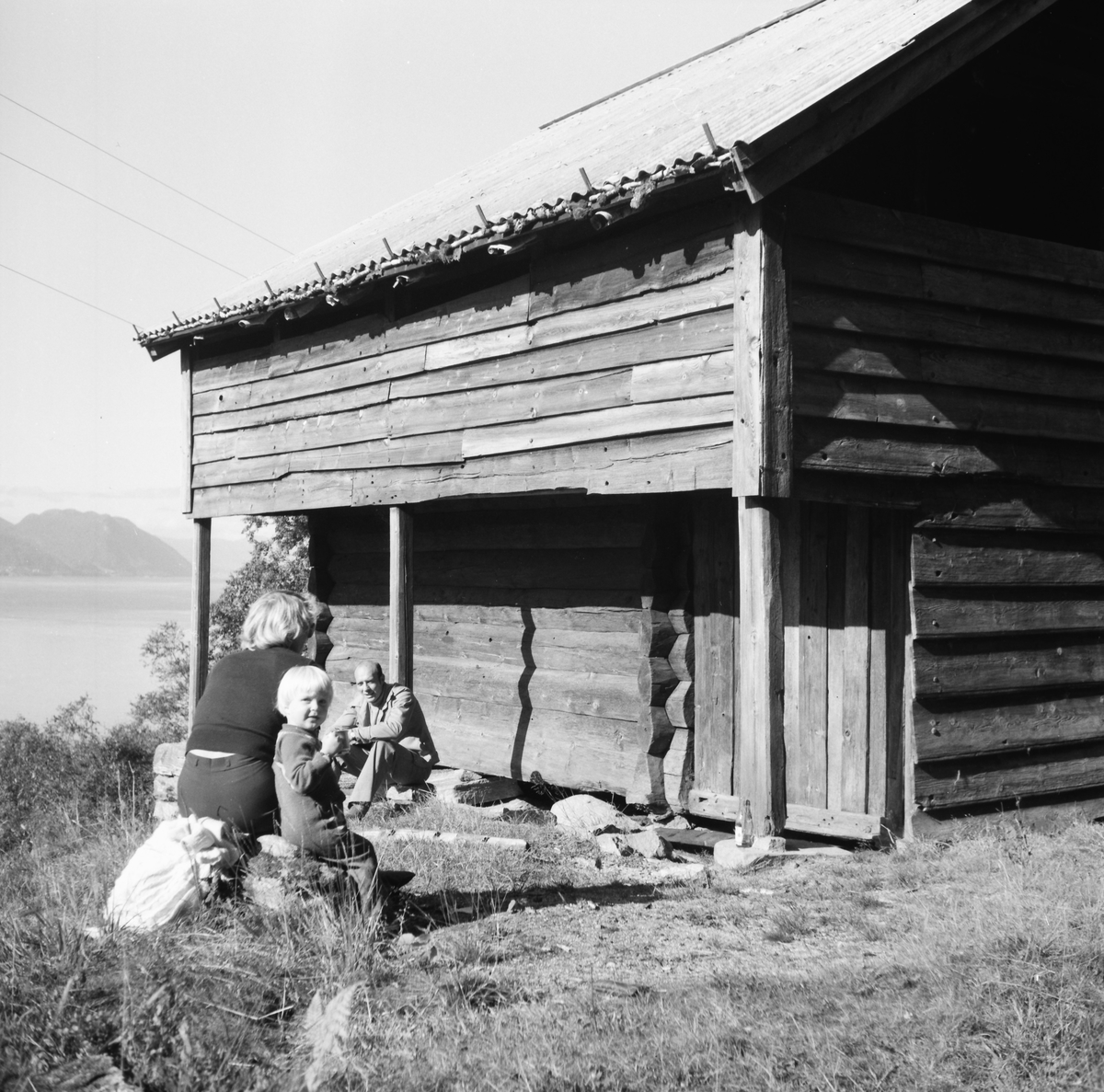 En familie på besøk ved Volda bygdetun. De er fotografert foran sengabuda. I tillegg er Kalvasstova(3) og Kornbergstova(4) fra tunet avbildet.