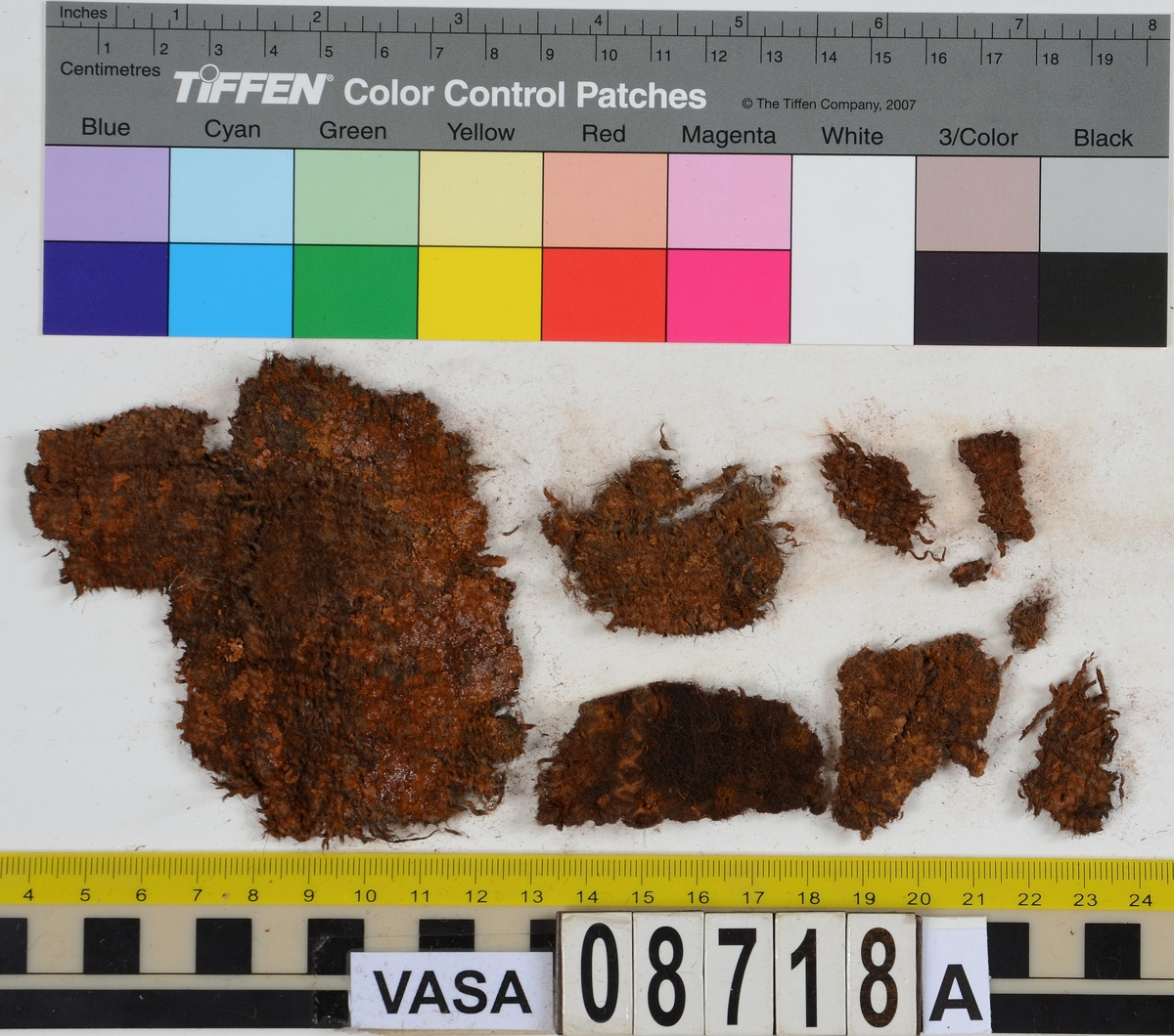 Textilfragment.
12 textilfragment uppdelade på fyndnummer 08718a-c.
Fnr 08718a består av 9 fragment av ull vävt i tuskaft och valkat. Ett av fragmenten har rester av en söm.
Fnr 08718b består av ett fragment av ull vävt i 2/2-kypert.
Fnr 08718c består av 2 fragment av ull vävt och med knutar på väven i en rad. Eventuellt är detta ett fragment från en rya.