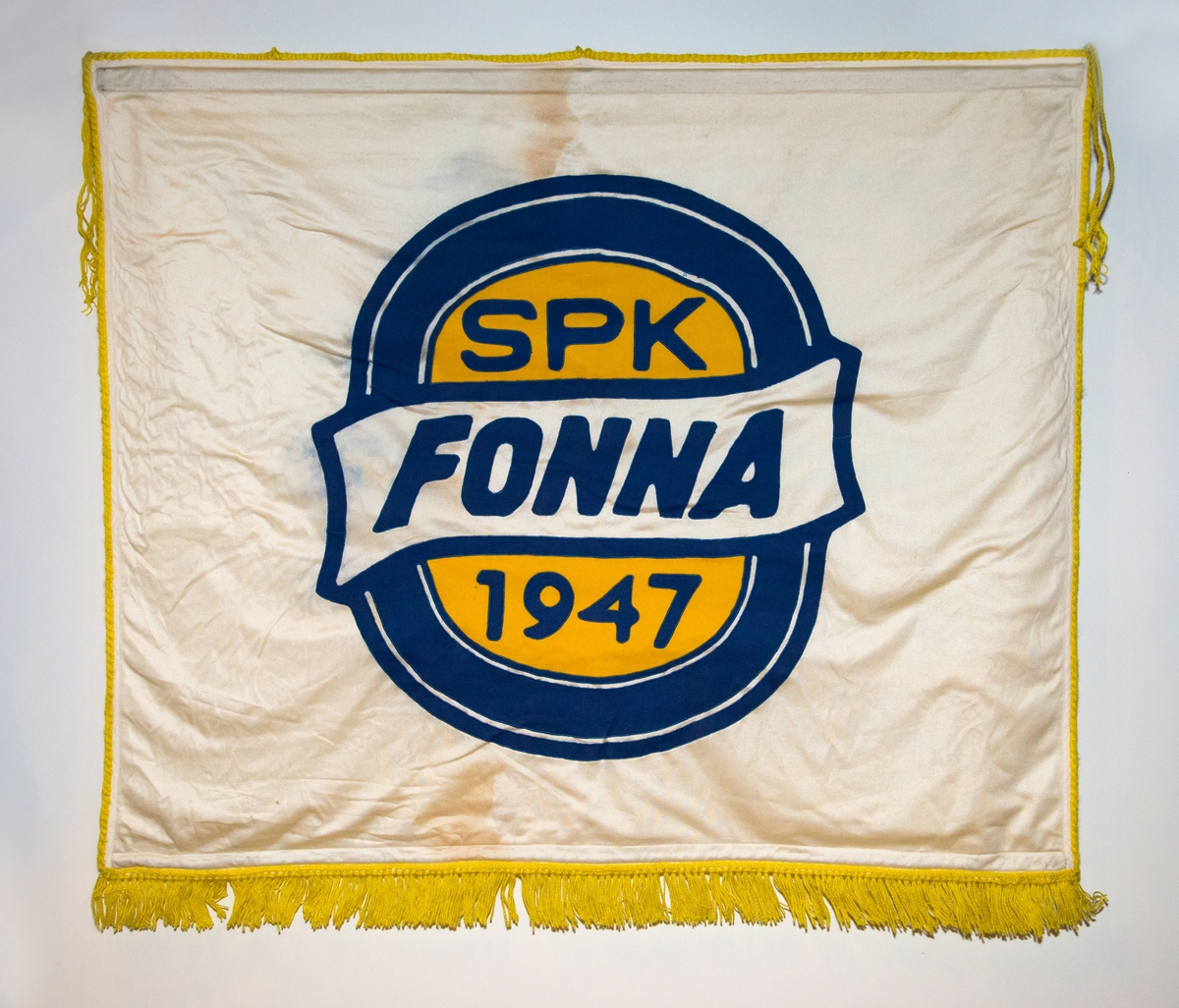 Motiv på ei side av fana er logo for sportsklubben Fonna: blå oval sirkel, gul inni, kvit vimpel med teksten FONNA på tvers av sirkel