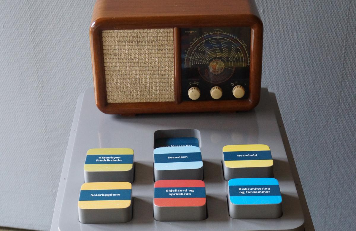 En radio fra 40-50-tallet, med 6 klosser foran. Klossene inneholder ulike lydklipp fra arkivene og handler om romanifolket/taterne og bosetting