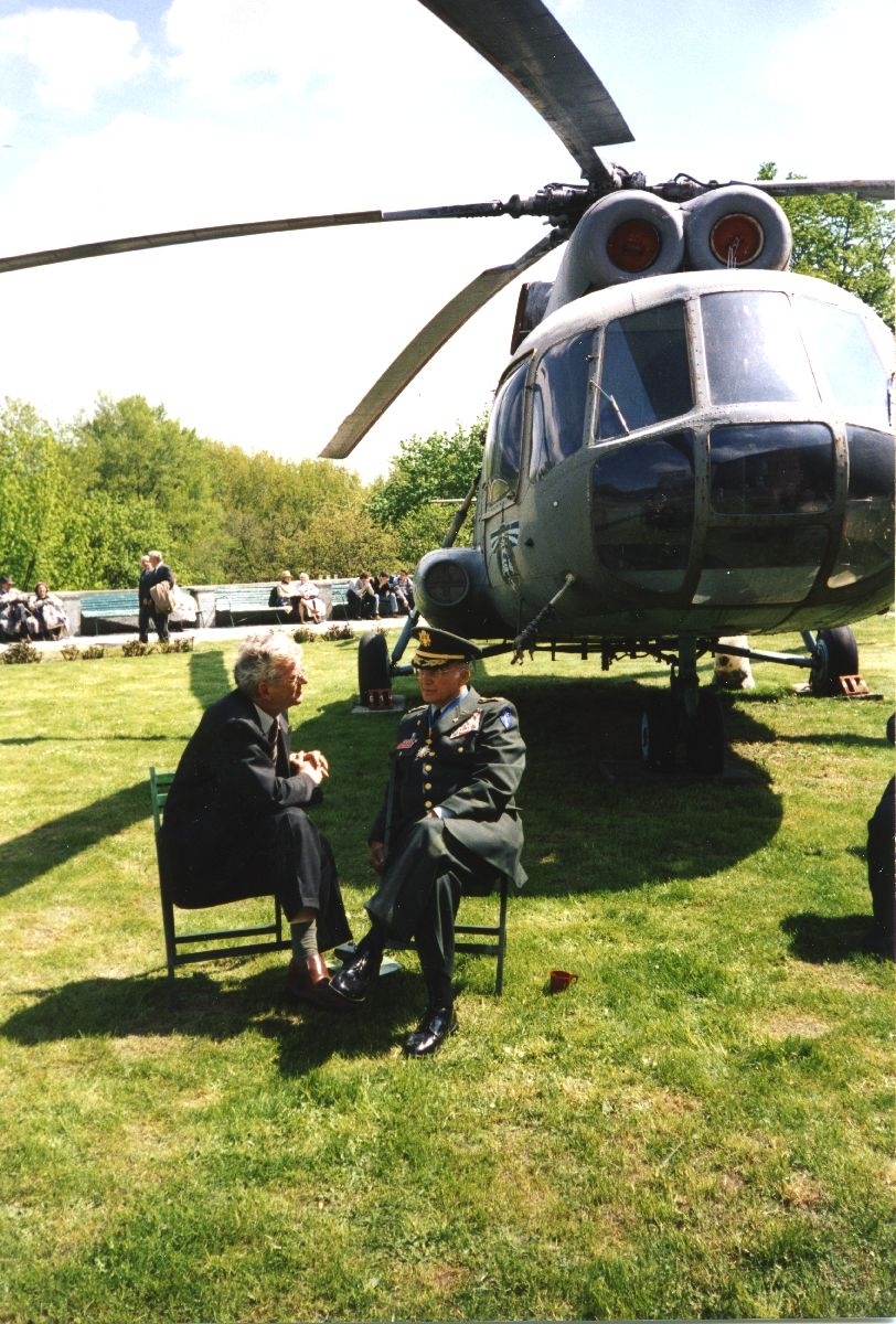 Landskap. To personer, den ene i uniform, i samtale foran et helikopter. Dette er ett av objektene som står oppstilt på et utstillingsområde for flyinteresserte besøkende.