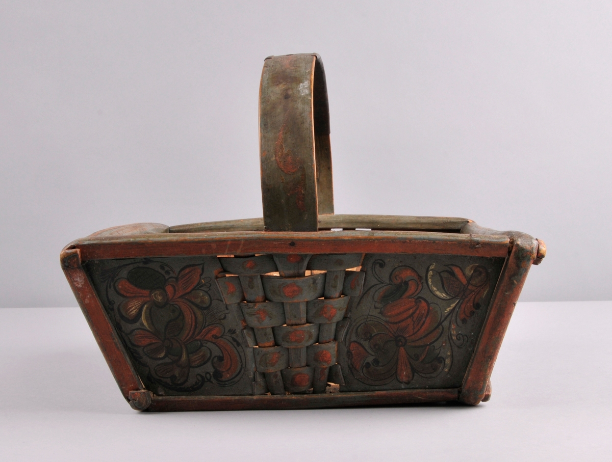 Sendingskorg, grøn botnfarge med rosemåling i fargane: kvit, raud, brun og svart. Initsialar er måla oppe på handtaket. Fletting med spon midt på alle sider. Hanka er forsterka med eit metallband som er festa med fire naglar.