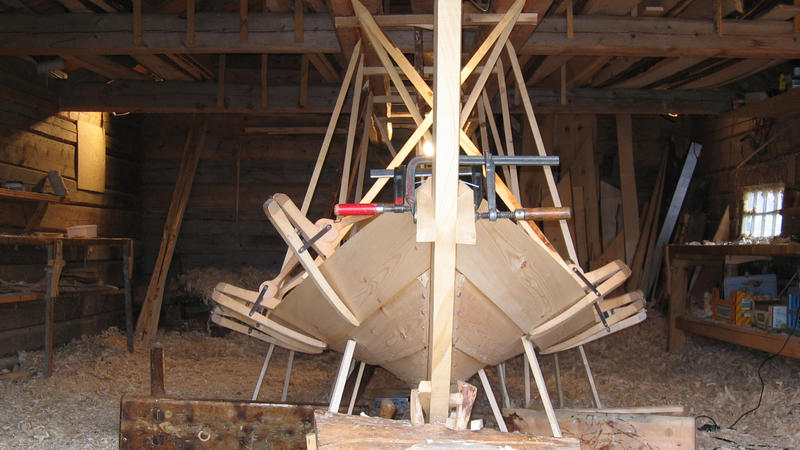 Clamps are used for holding the new strake in place before it is properly fastened. The sticks pointing down from the ceiling and up from the ground are used to shape the boat, by applying more or less pressure in different areas. (Foto/Photo)
