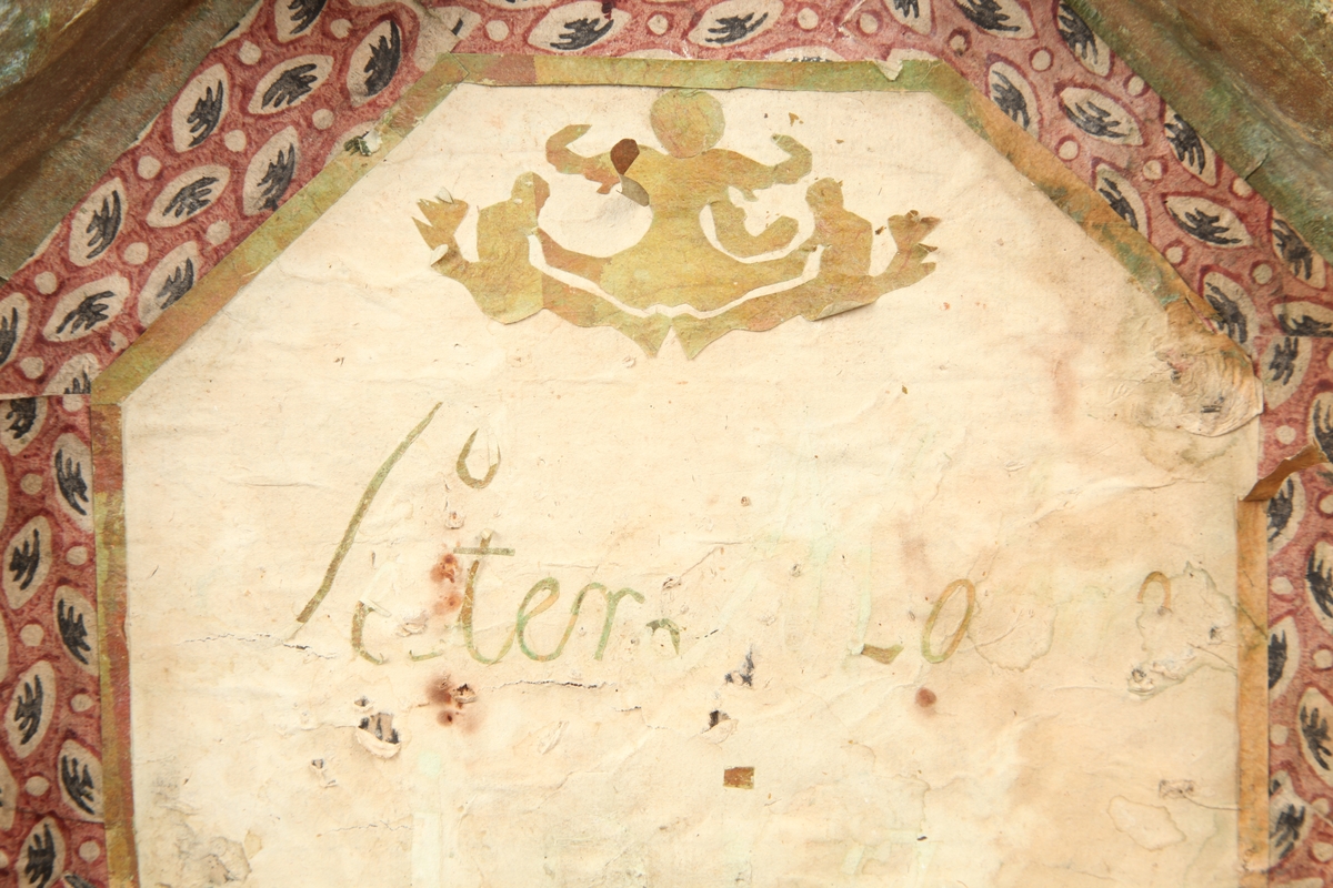 Åttekantet. Den har dekorerte flater i messing med jernbeslag og det hele er naglet på tre. På lokket er det en hank. Flaskefôret er låsbart, men den originale nøkkel mangler.