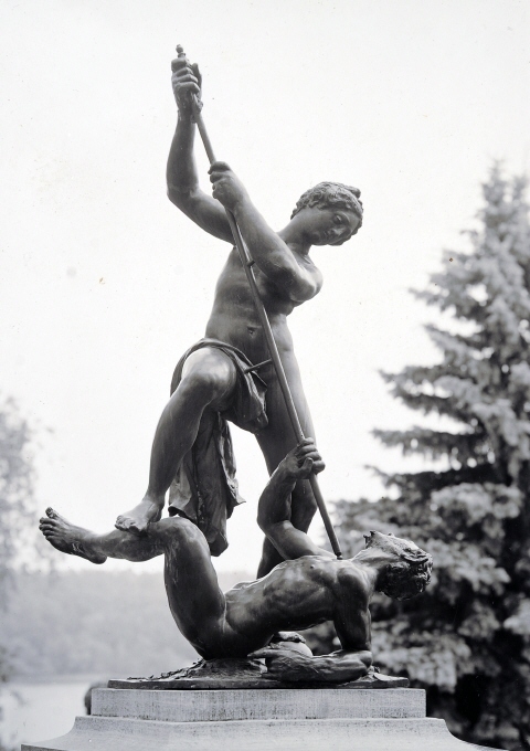 En stående kvinnlig figur håller med bägge händerna ett spjut, som hon stöter mot bröstet av en liggande man. Hon håller huvudet något nedåtböjt fas höger, överkroppen något fas vänster. Över det högra benet ett skynke, i övrigt naken. Står med vänster fot på ett klot och stöder höger på mannens vänstra upplyftade ben. Mannen, som bär ett kort skägg, ligger stödd på vänster armbåge och håller med höger hand i spjutet. Han är helt naken. På den fyrkantiga plinten förutom klottet ett armband, omgivet av vallmofröhus samt i relief blommor, grenar och blad.