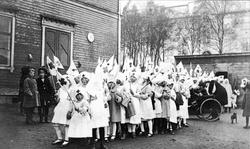 Opptog med barn kledt ut som sykesøstre. Byskolen i bakgrunn