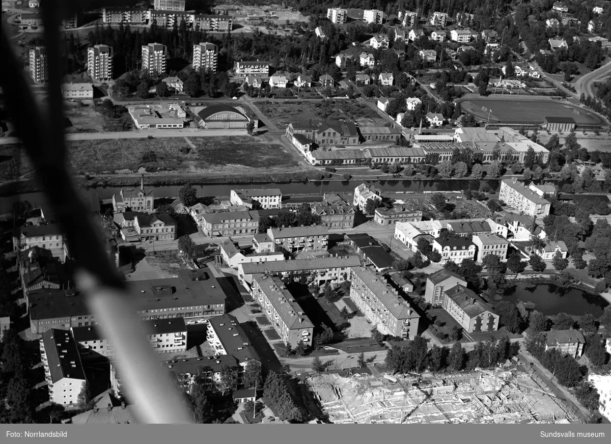 Flygfoton över västra Norrmalm med Alliero, tennishallen, Epidemin, Sundsvalls verkstäder. Påbörjat bygge av bostäder vid Ludvigsbergsvägen 12-20 och på en av bilderna syns det påbörjade bygget av Åkersviksskolan i nederkanten.