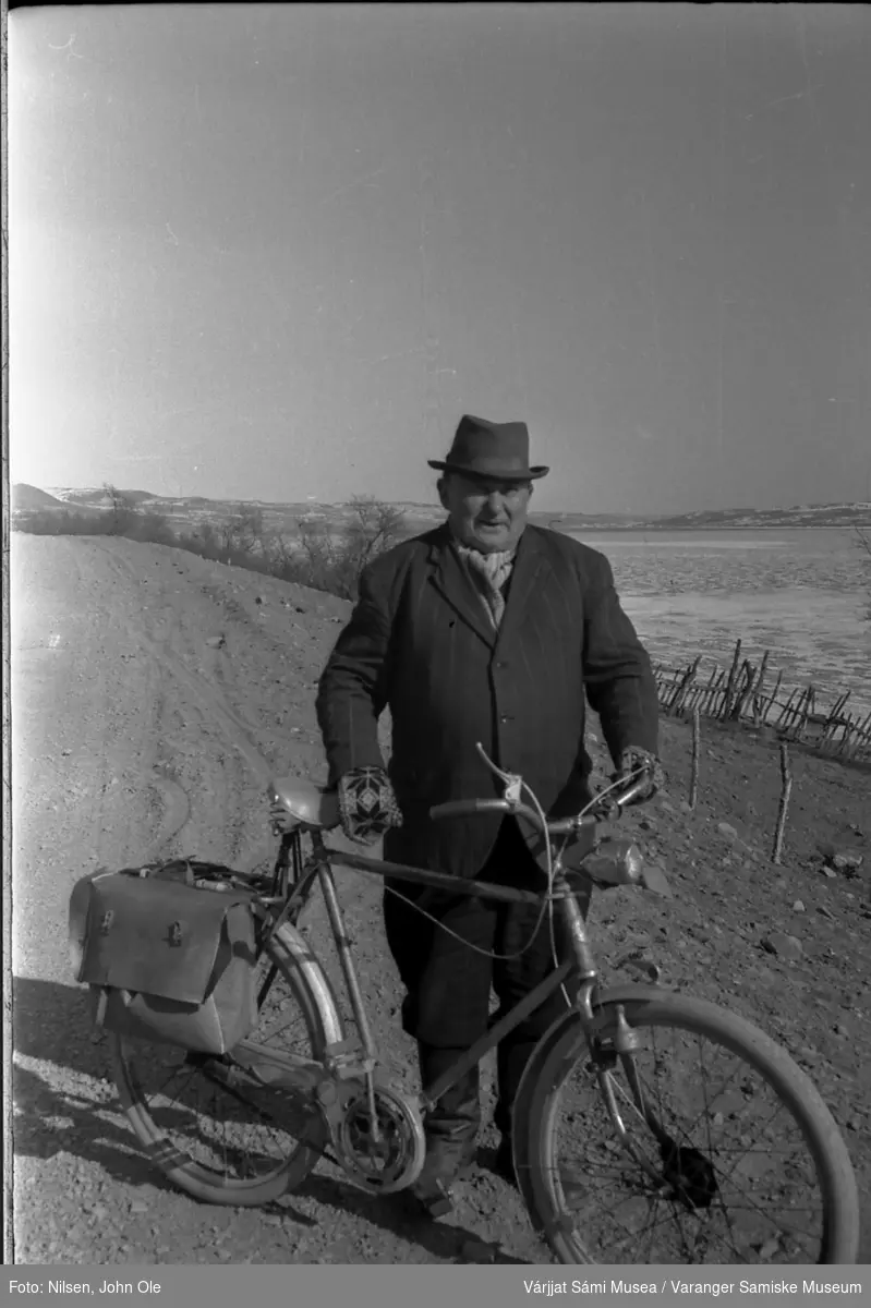 Ole Oksehode (Borr-Ovla) med sykkel. Bildet er tatt rett nedenfor tidligere Amtmannsgammen museum i Varangerbotn, Varangerfjorden i bakgrunnen. April 1967.