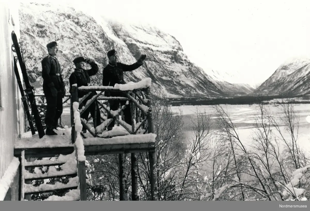 Tre soldater som ser på noe til høyre for bildet. I bakgrunnen ser vi Sunndalsøra og litt av fjorden. Dei står på ein veranda til eit hus som mest sansynlig ligg på Viklandet.