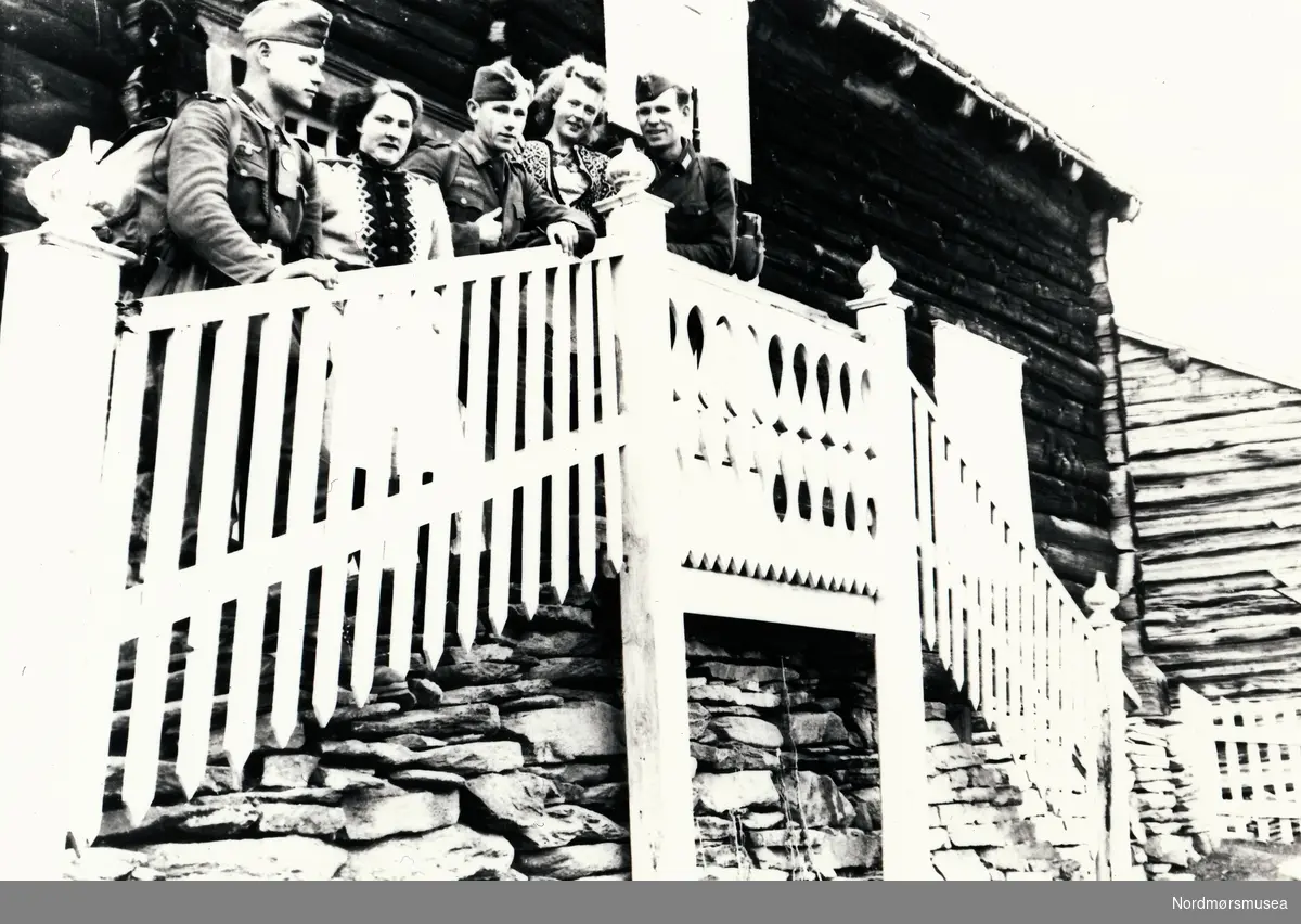 Tre soldater og to kvinner stå i trappa ved inngangen til eit hus.