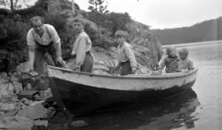 Fire barn ombord i en båt som ligger ved land. En mann står 