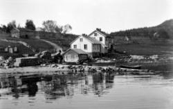 Foto av et hus nede ved sjøkanten med gårdbruksareal i bakgr