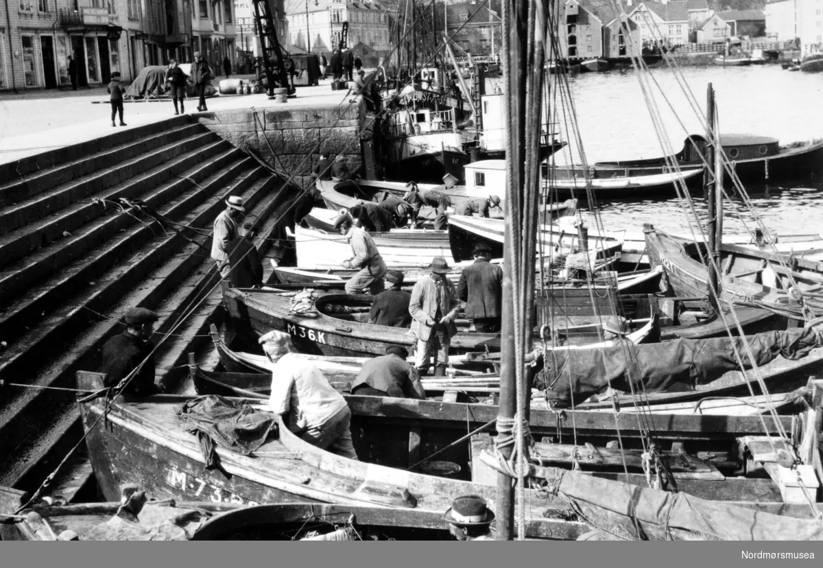 Foto fra Anders Beer Wilses fotoarkiv, hvor vi ser fra fisketrappa ved fisketorvet på Kirkelandet i Kristiansund. båtene tett i tett for å selge dagens fangst. Fotoet er trolig fra perioden rundt 1910-1930. Fra Nordmøre Museums fotosamlinger.

