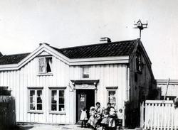 To kvinner og seks barn i solveggen utenfor inngangen til Gr