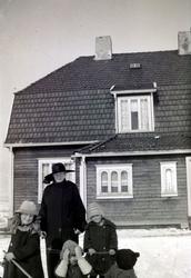 Foto av en kvinne og tre små barn foran en villa en vinterda