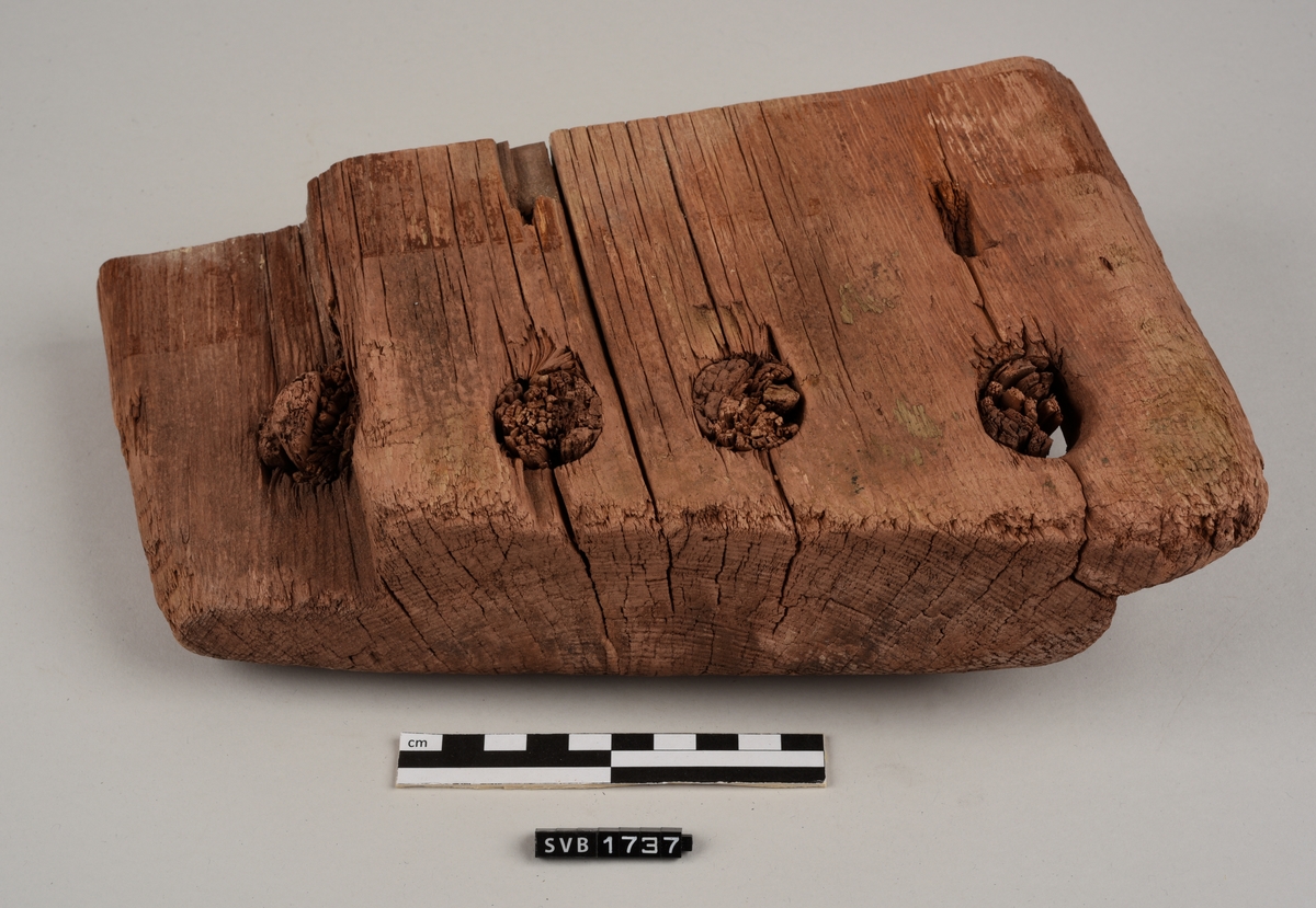 Del av bord til sydd båt. Det er hull med treplugger og sømhull med søm av røtter. Trematerialet har en rødlig farge. Antakelig på grunn av fargen på sanden der den var funnet.