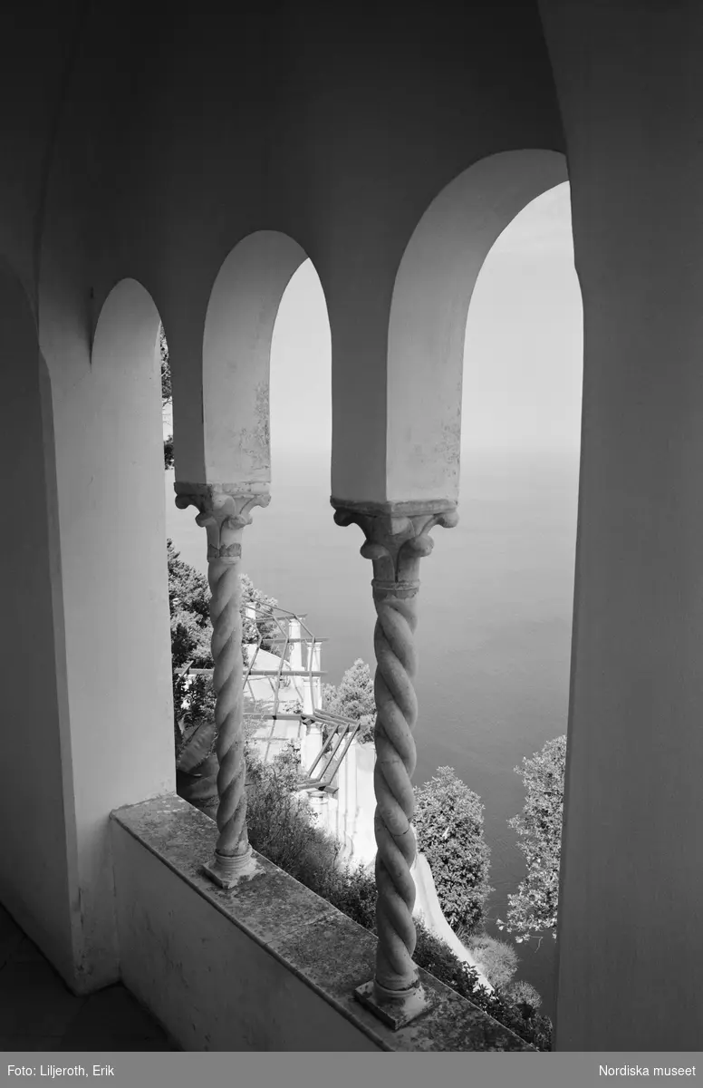 "Utsikten från cubiculum ner mot pergolan och längst ned Neapelgolfen är med rätta berömd som en av jordens skönaste." Vy från Axel Munthes villa San Michele. Mellan valv uppburna av två spiralformade kolonner syns vatten och träd.