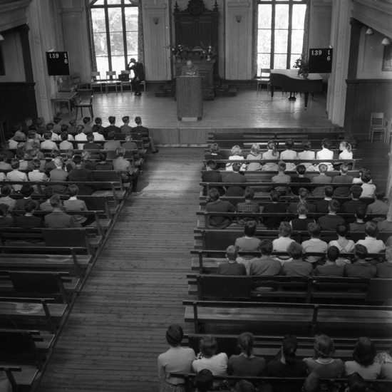 En man står i en talarstol och håller tal inför skolelever. Aulan,
Växjö Högre Allmänna Läroverk. 1958.