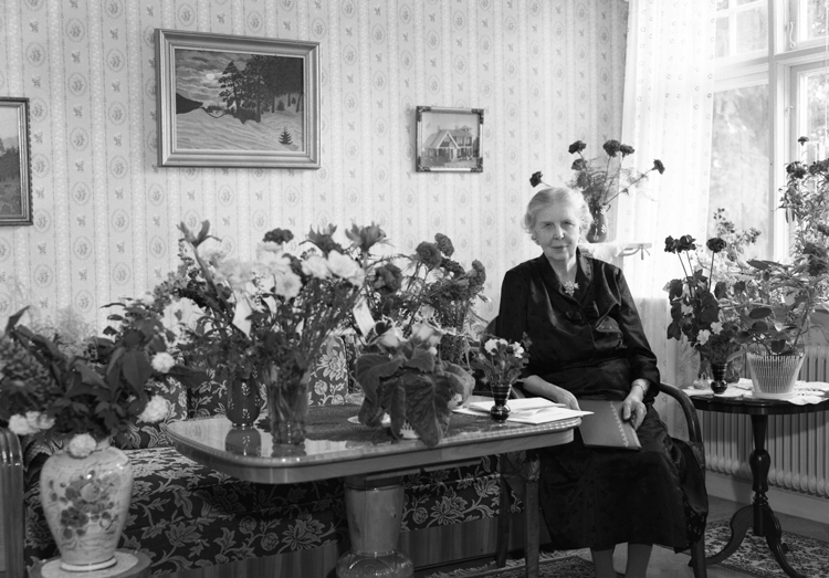 Foto av en äldre kvinna som sitter i ett vardagsrum, omgiven av blommor. 

Fröken Anna Sofia Wahlberg (11 juni 1881-1973), Alvesta. 
Källa: Sveriges Dödbok 1901-2009.