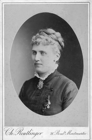 Porträttfoto av Christina Nilsson. Hon bär klänning  med en brosch vid halsen och några slags 
medaljonger vid bröstet
