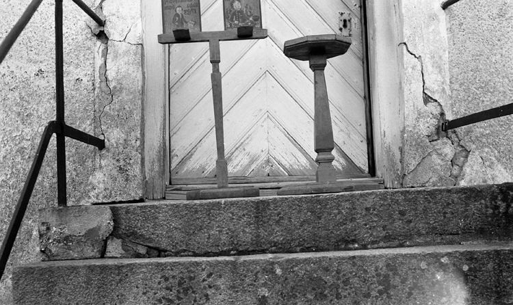 Foto i en kyrktrappa med en dörr bakom. På trappan står en piedestal  och ev. ett  notställ (?), psalmboksställ (?).