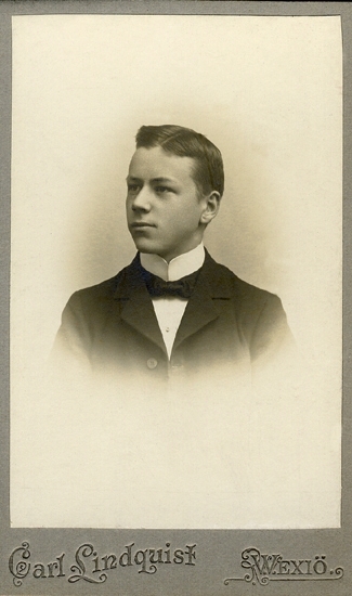 Porträtt (bröstbild, halvprofil) av en okänd ung man i mörk kavaj och vit skjorta med hög stärkkrage och mörk fluga.