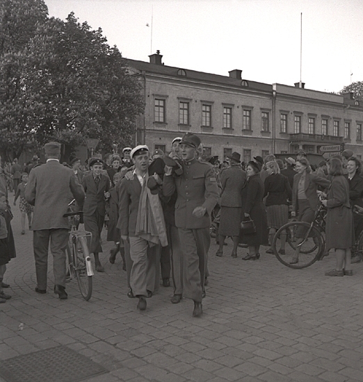 Studenterna 1940. 31/5 - 1/6. En manlig student bärs av sina kompisar längs Stortorget. I bakgrunden syns Residenset.
