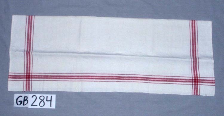 Handduk. Handvävd.
Kvalitet: halvlinne, bomull i varp (dubbelt) , lin i inslag.
Fållar: 0,6 cm, handfållade.
Hängband: handvävt, vitt med röd rand, 0,8 cm brett, 
5 cm långt, 2 st.
Varpordning till bård:
Rött:    2 6 6 2
Oblekt:  6 2 6
Inskrivet i huvudkatalogen 1996-1997.