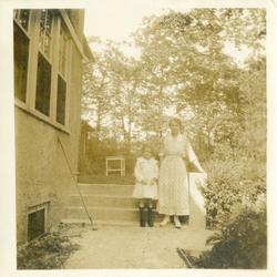 Kvinne og jente ved ei trapp utenfor et hus. Kvinna har lang