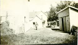 Bildet viser et tun med to hus og en garasje. En mann går ov