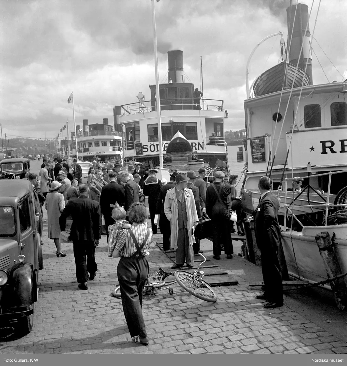 Nybroviken, Stockholm. Folksamling på Nybrokajen, skärgårdsbåtar i bakgrunden.